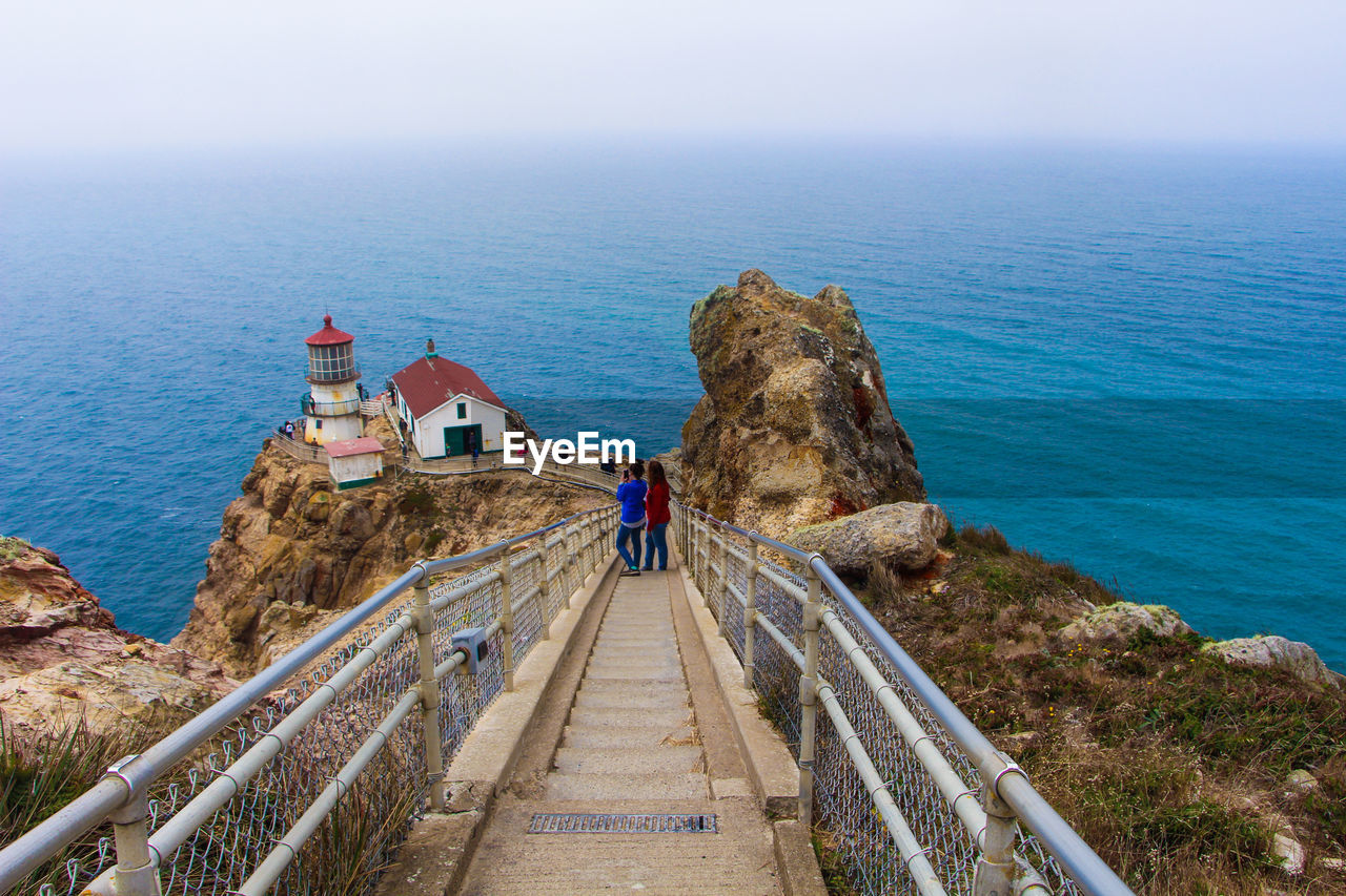 People standing on walkway by sea against sky