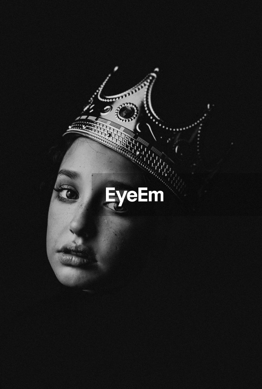 Portrait of young girl against black background with crown sitting shadows. notorious