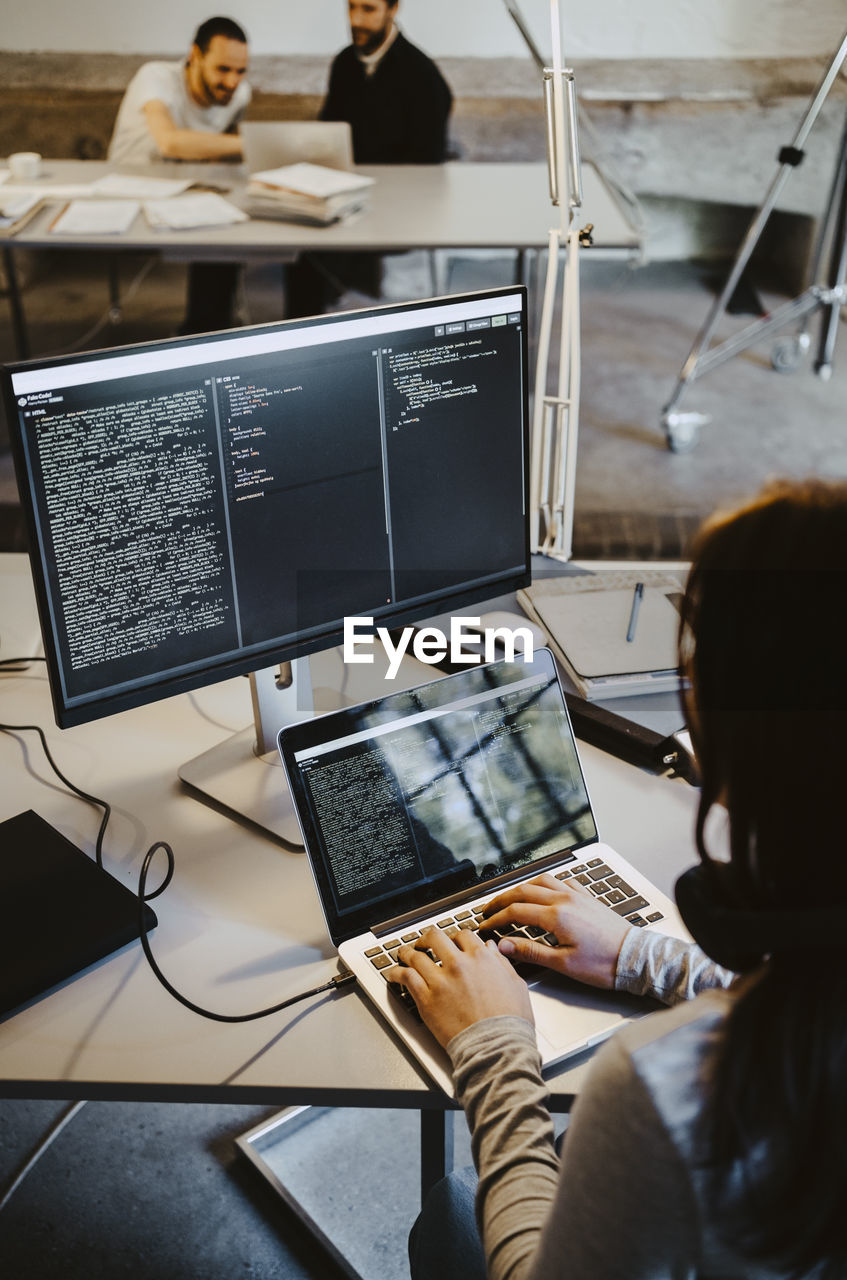 Female programmer coding on laptop at table in creative office