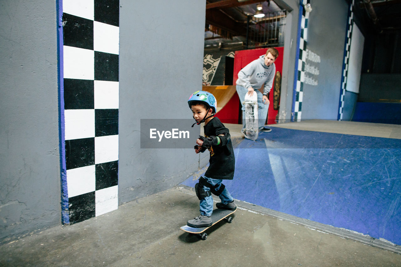 Skater kid looks focused after skating down a ramp, instructor watches