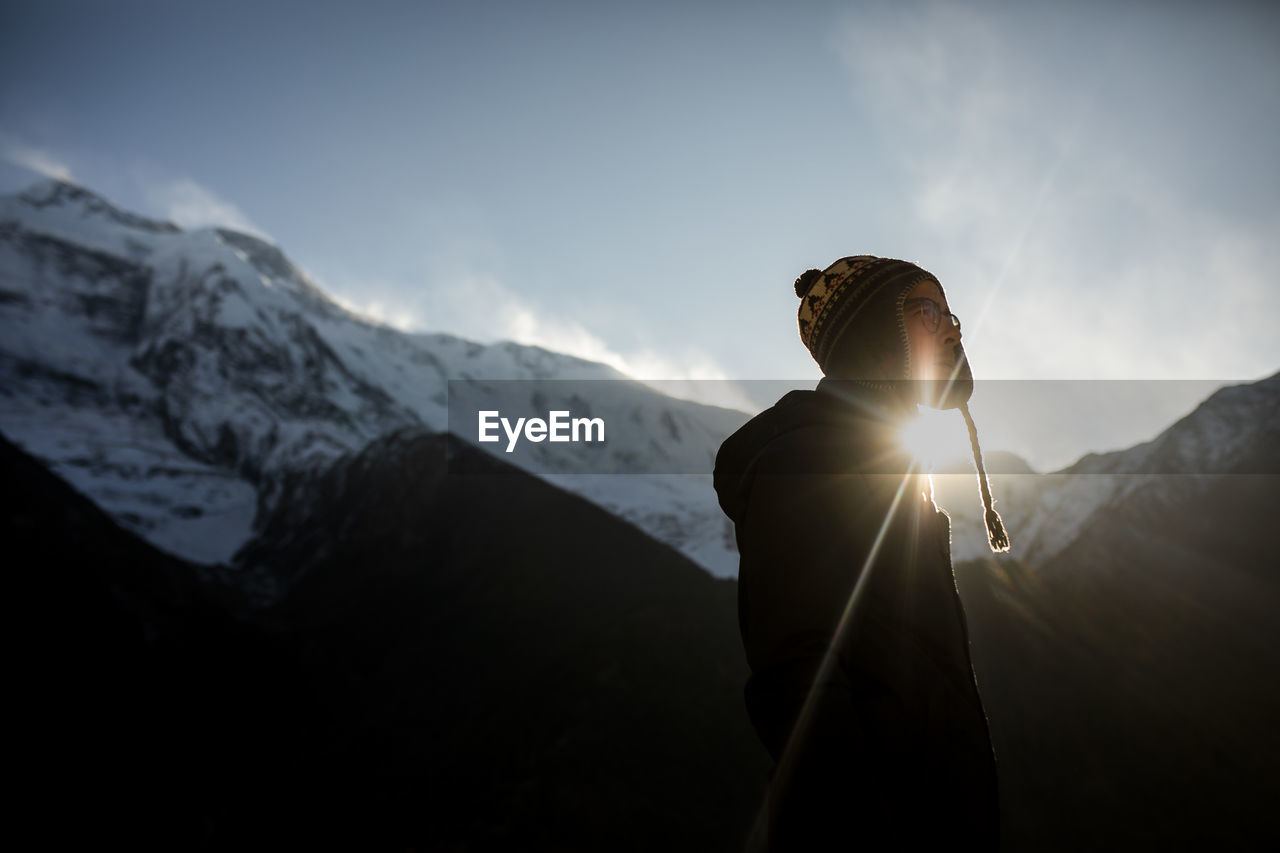 Side view of thoughtful male traveler in warm clothes standing on background of himalayas mountain range on sunny day in nepal