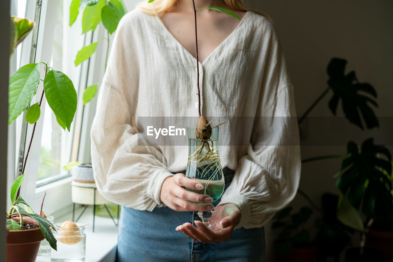 midsection of woman holding potted plant against wall