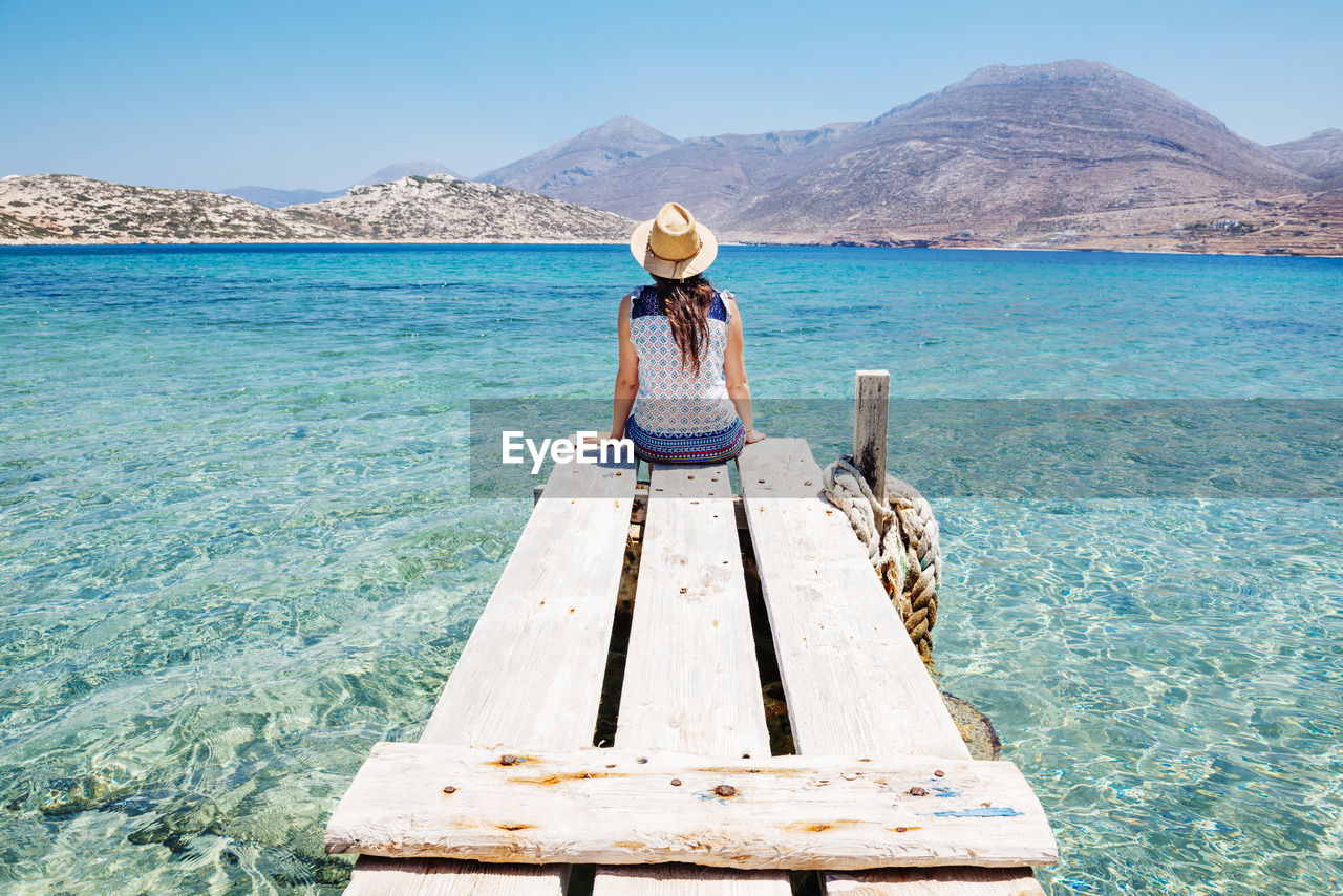 Greece, cyclades islands, amorgos, woman sitting on the edge of a wooden pier, nikouria island