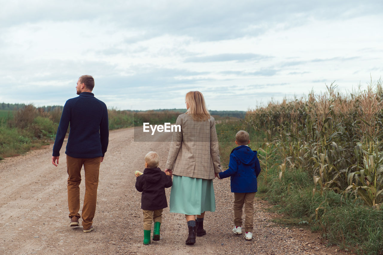 Family walking countryside road near corn field at autumn