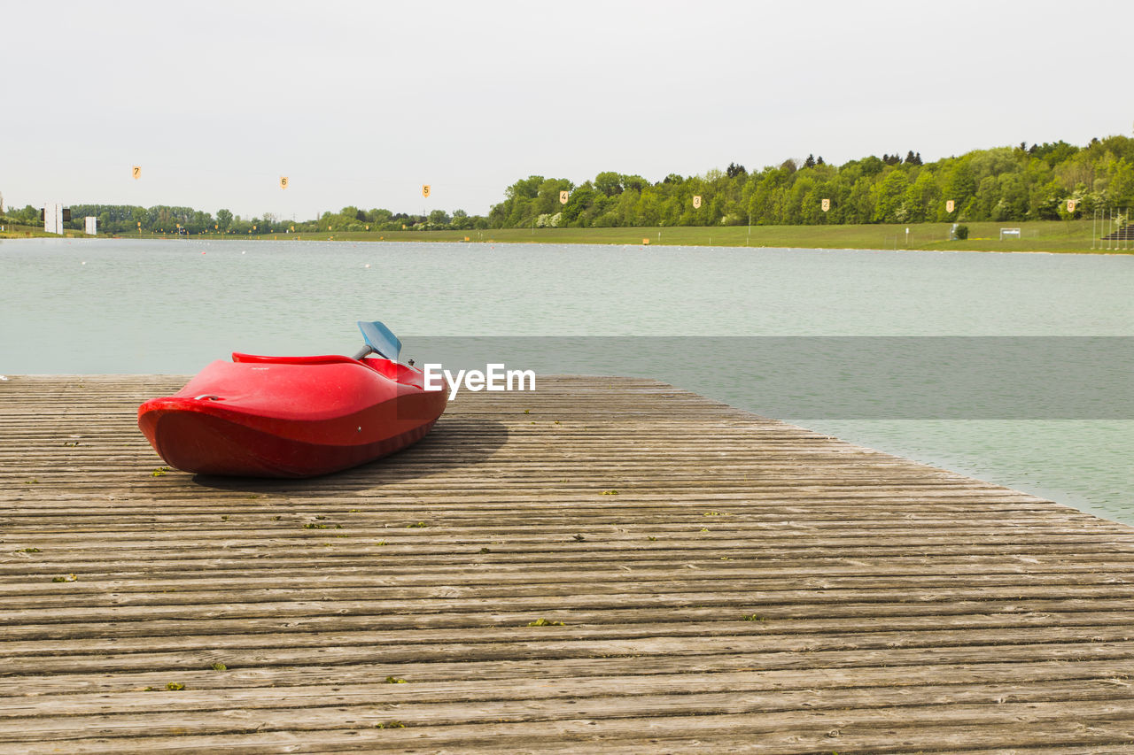 Red canoe on pier over lake against clear sky