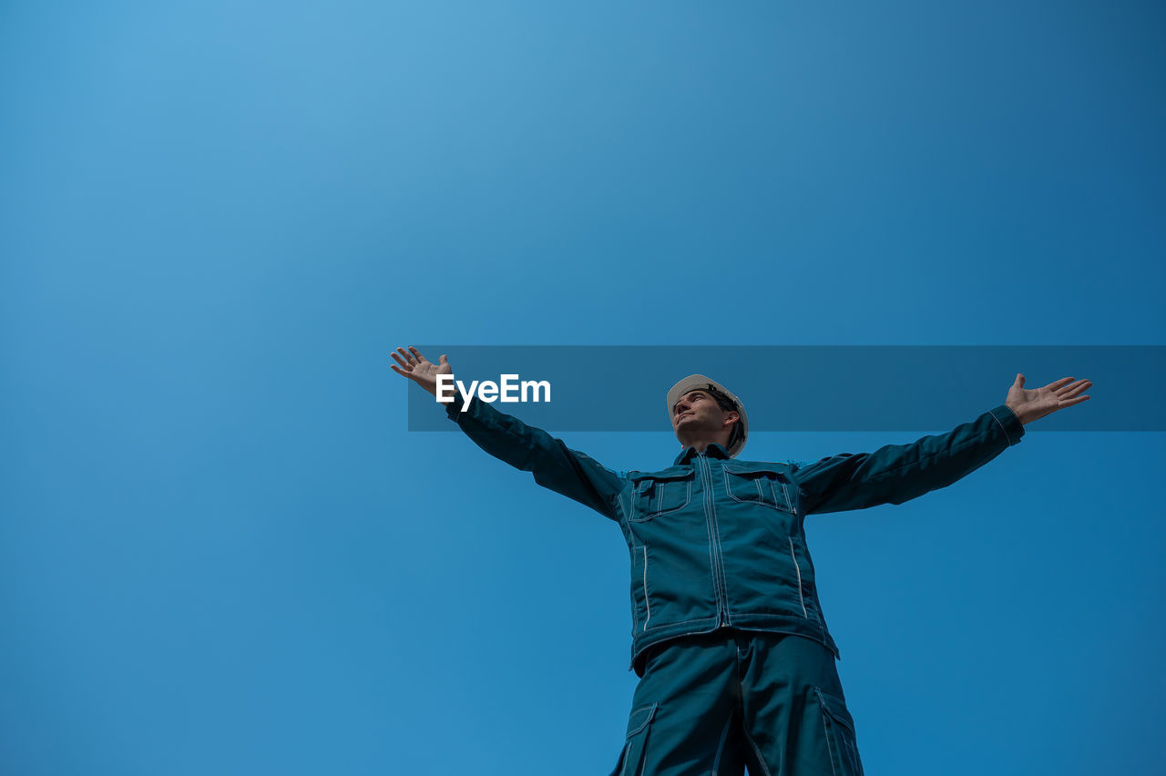 low angle view of woman with arms raised against clear blue sky