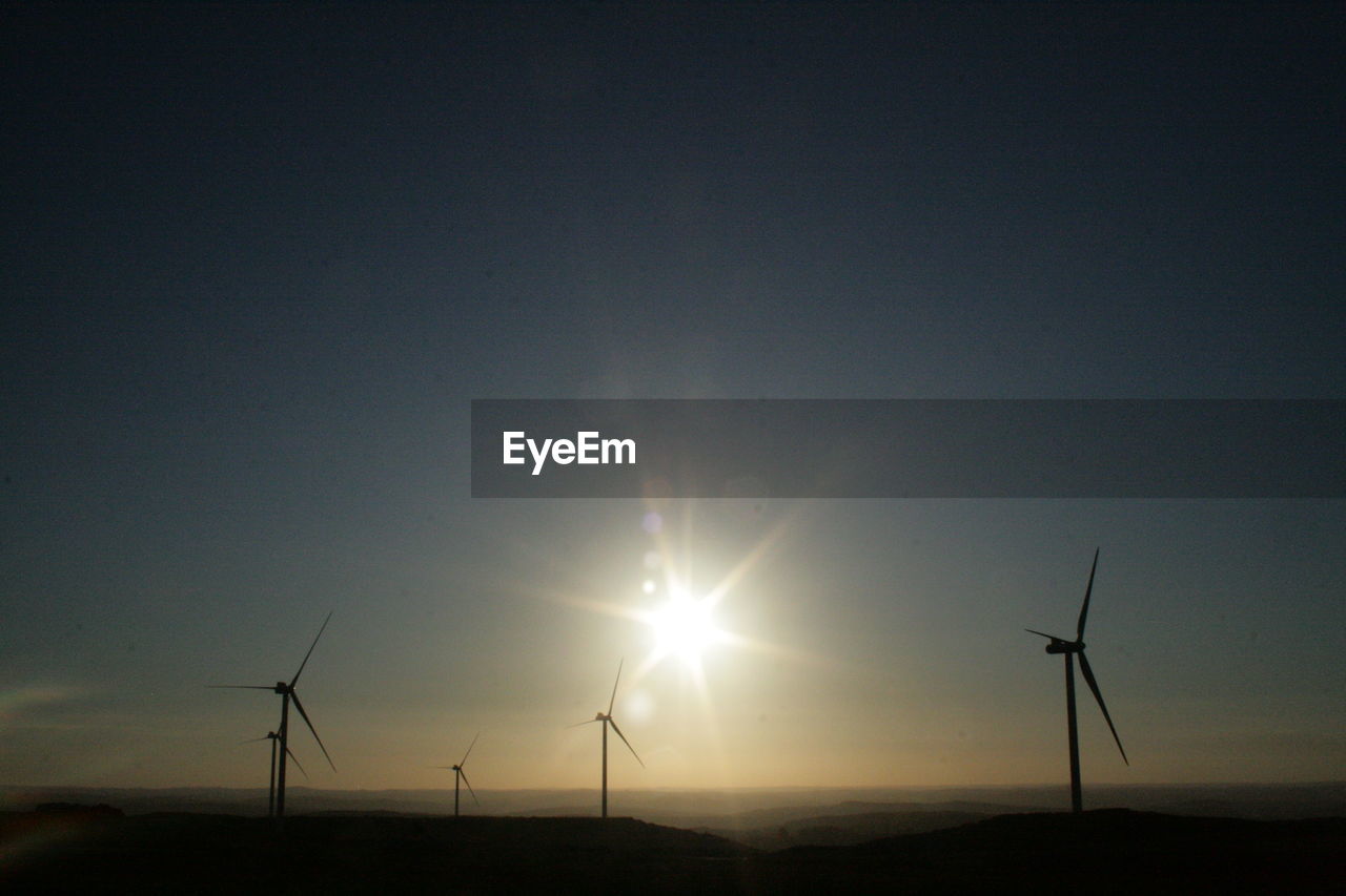 Wind turbines on landscape at sunset