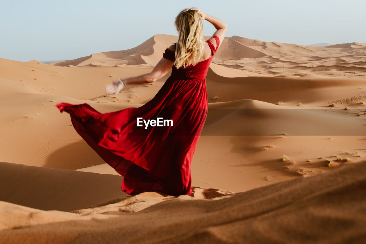 Young woman wearing red dress while standing at desert against clear sky