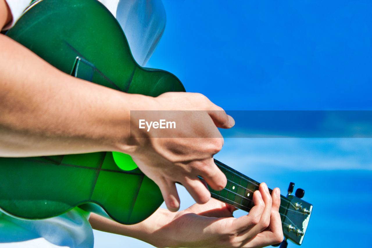 Midsection of person playing guitar against blue sky
