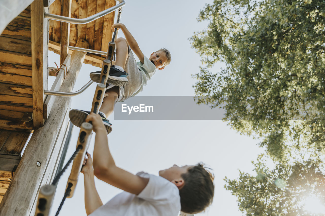 Brothers climbing ladder in public park on sunny day