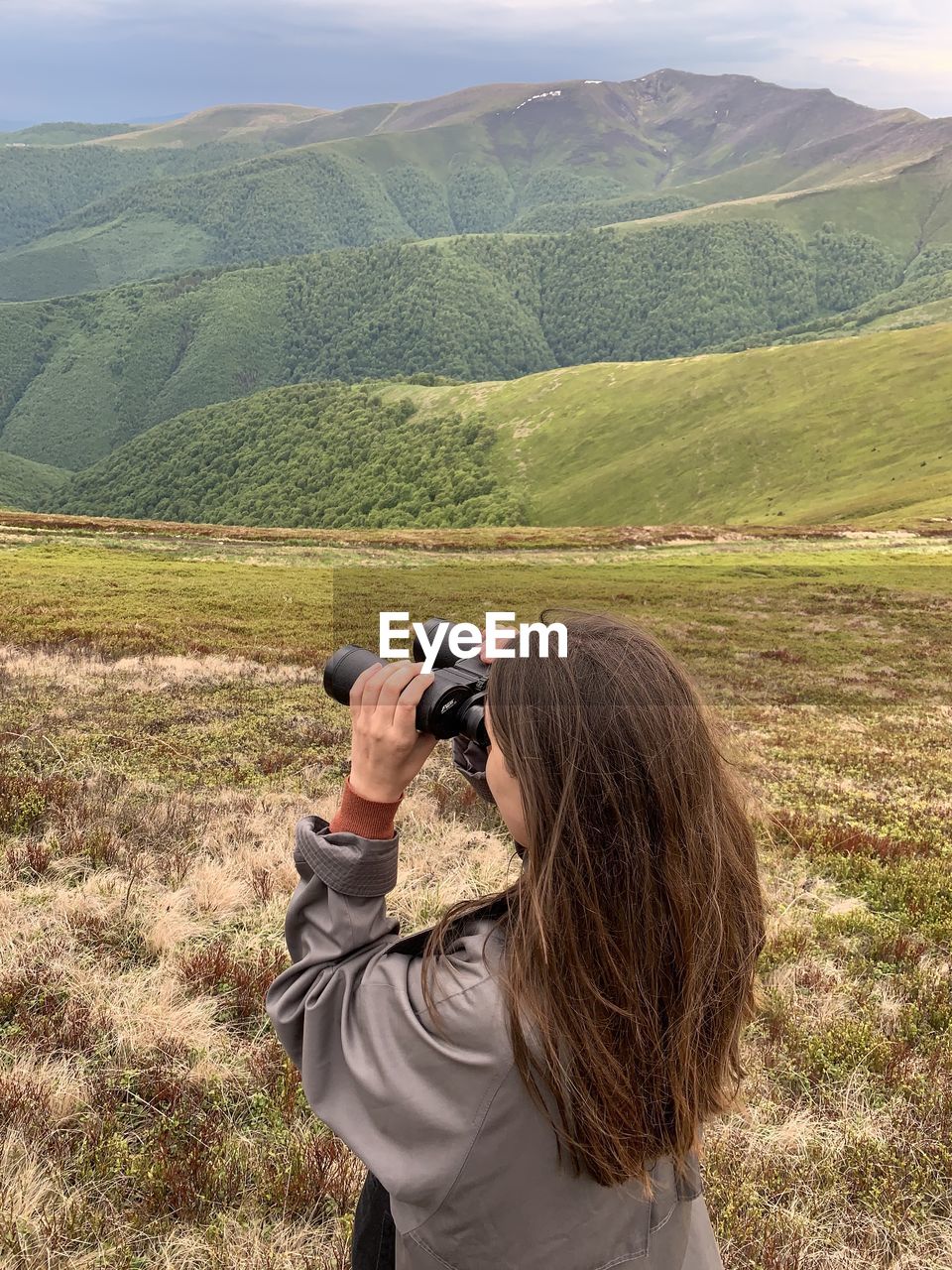 Rear view of a woman standing with binoculars in the mountains against the sky