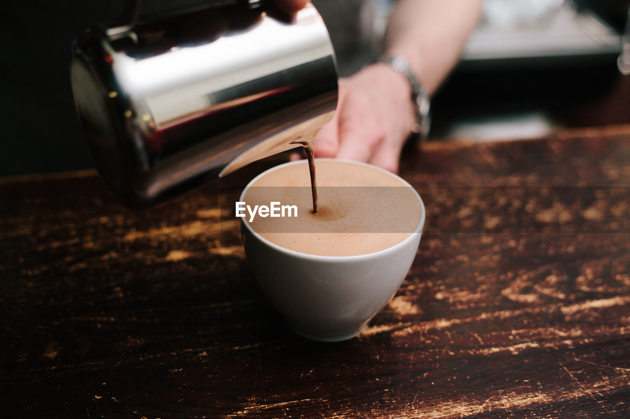 Cropped hand pouring coffee in cup on table