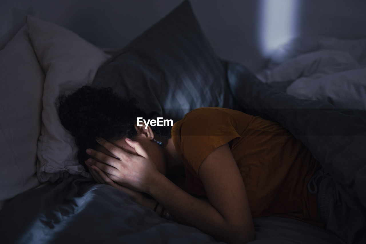 Crying young woman lying in bed