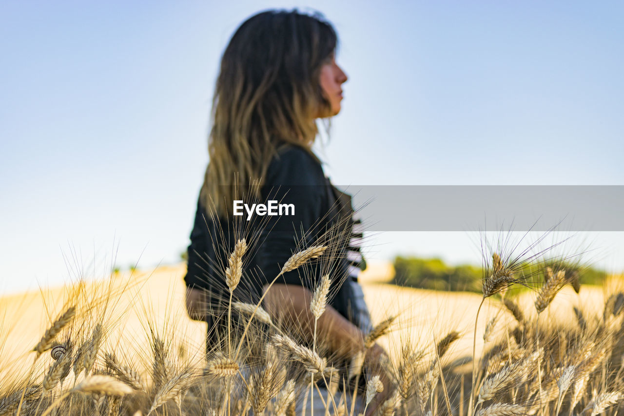 Side view of young woman in field against clear sky