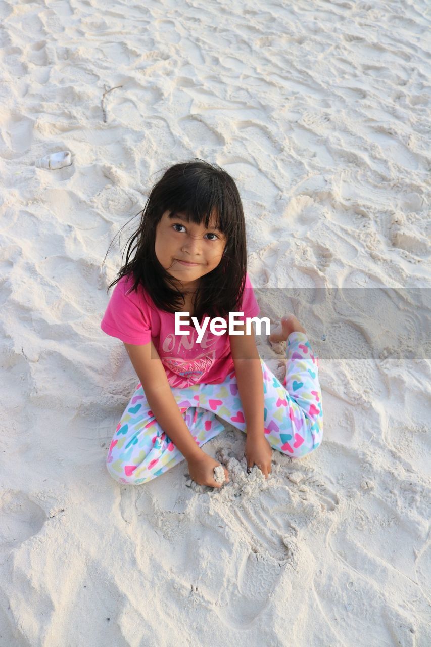 High angle portrait of girl sitting on sand at beach