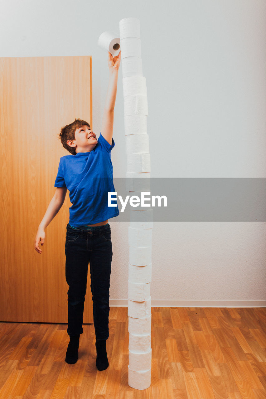 Boy stacking tissue rolls against wall