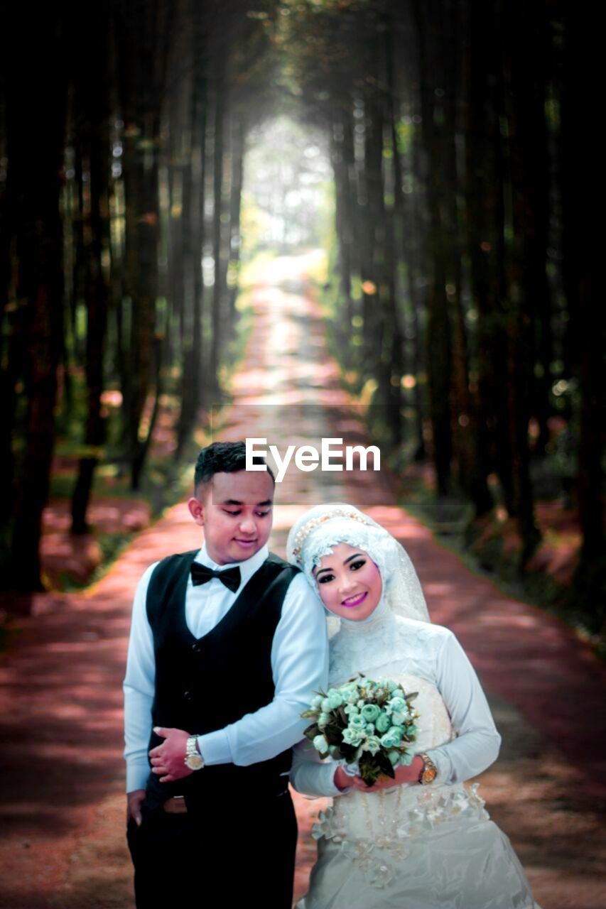 Bride and groom standing on footpath against trees