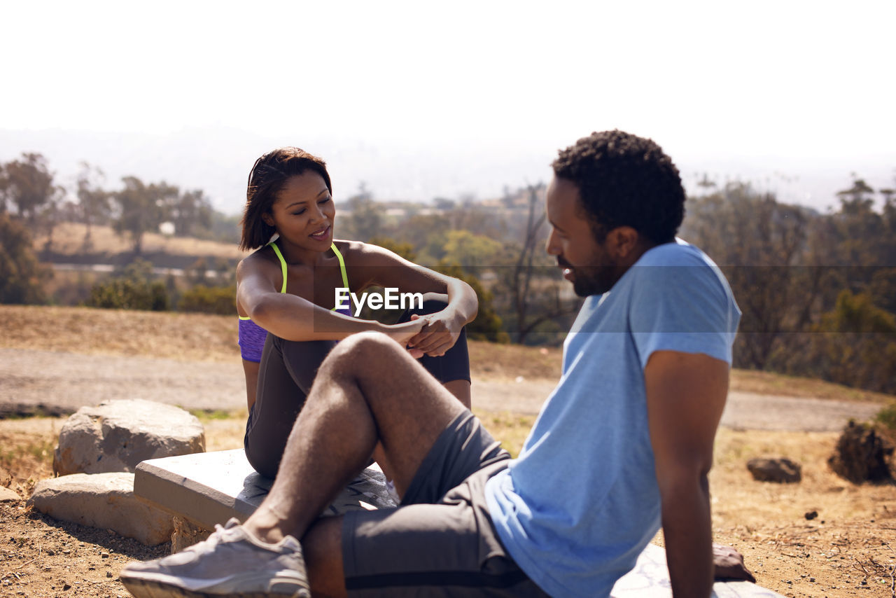 Joggers sitting on rocks at countryside during sunny day