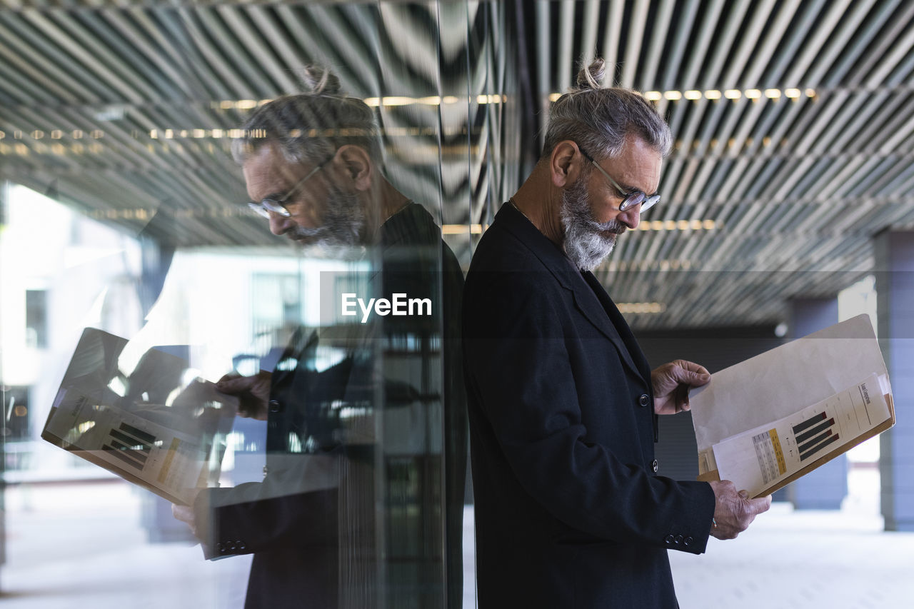 Hipster businessman reading business plan while standing in front of glass wall