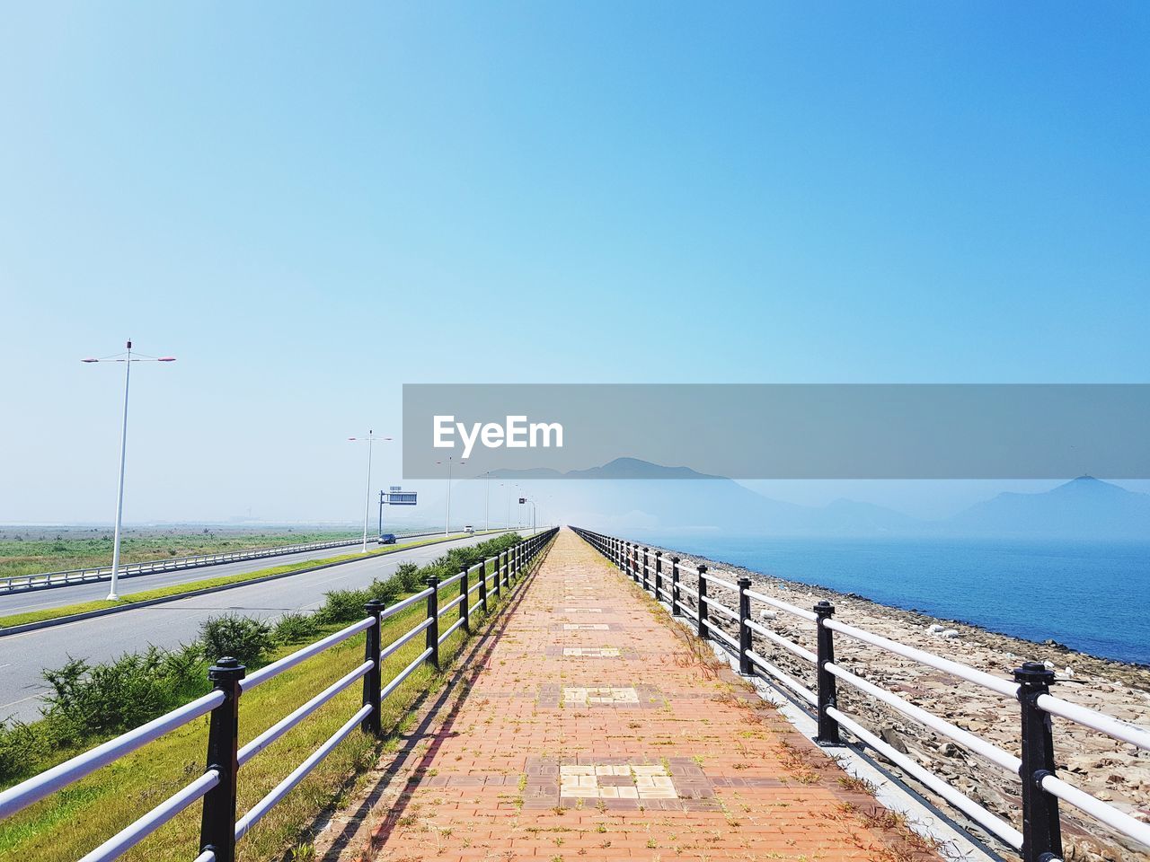 Walkway by sea against clear blue sky