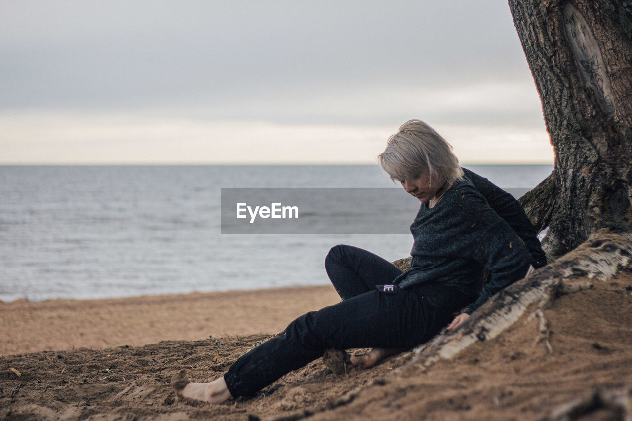 Young woman relaxing on sand at beach against sky