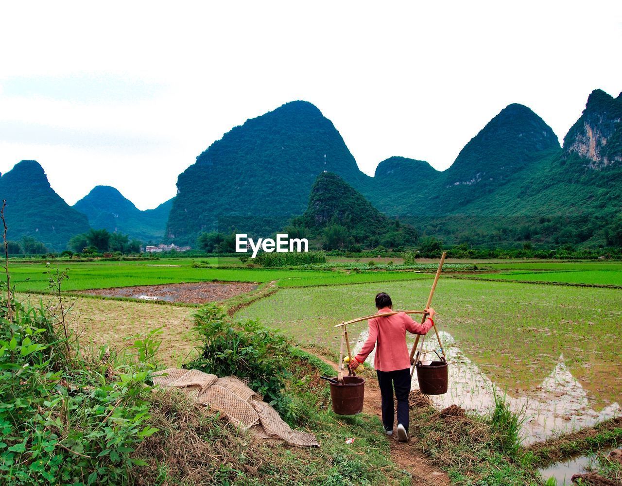 REAR VIEW OF MAN STANDING ON LANDSCAPE AGAINST SKY