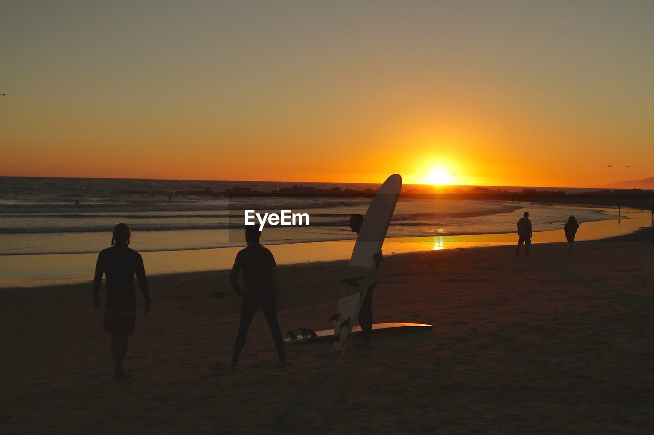 Friends enjoying at beach against clear sky during sunset