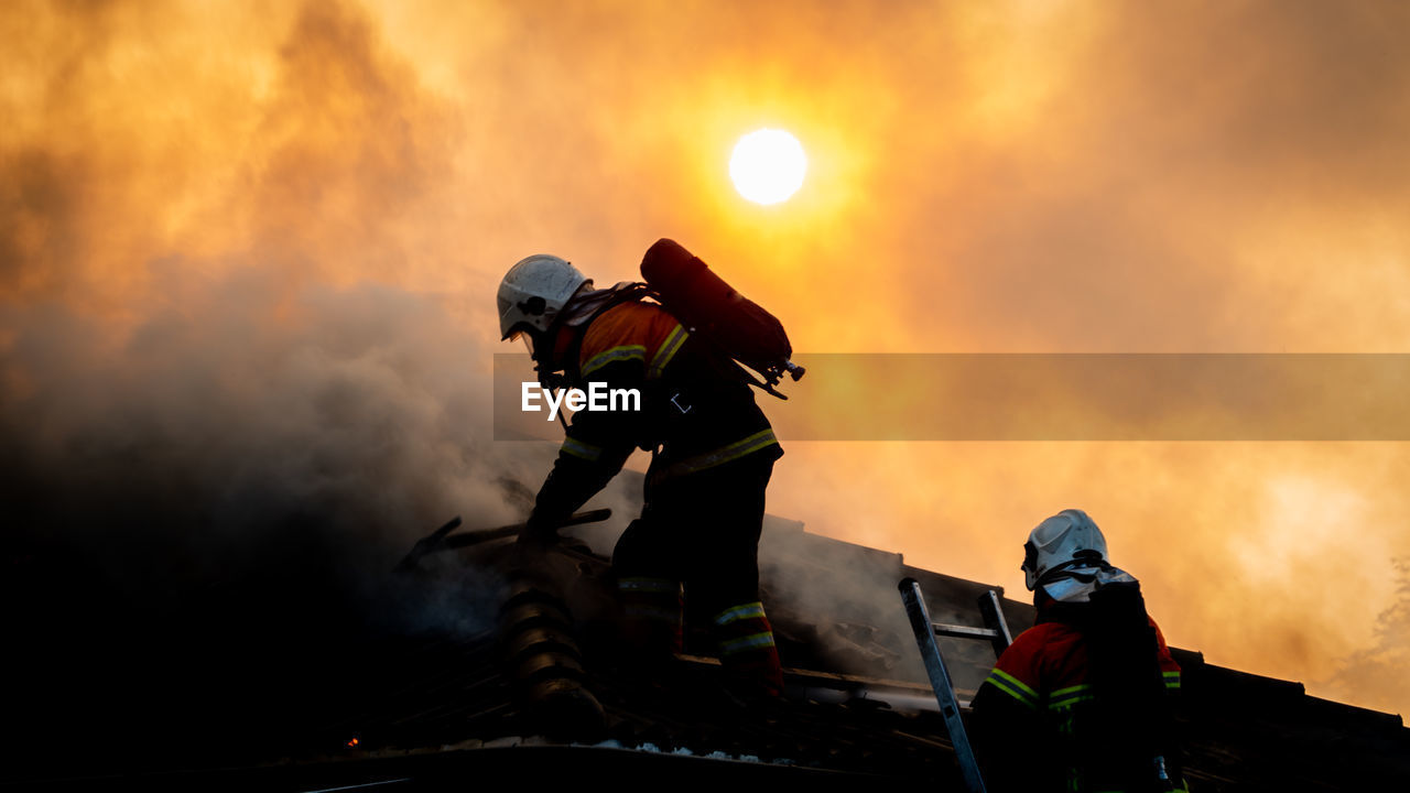 Man working on fire against sky during sunset