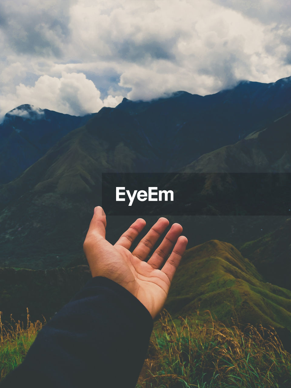 Cropped hand of person gesturing against mountains and sky