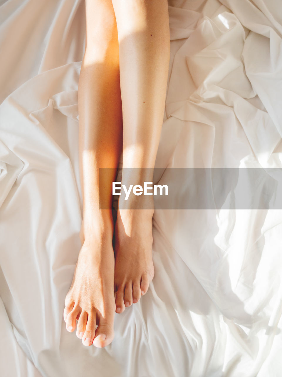 Morning bedtime. woman's feet on unmade bed. sunbeams on white crumpled bed sheet. light and shadow.