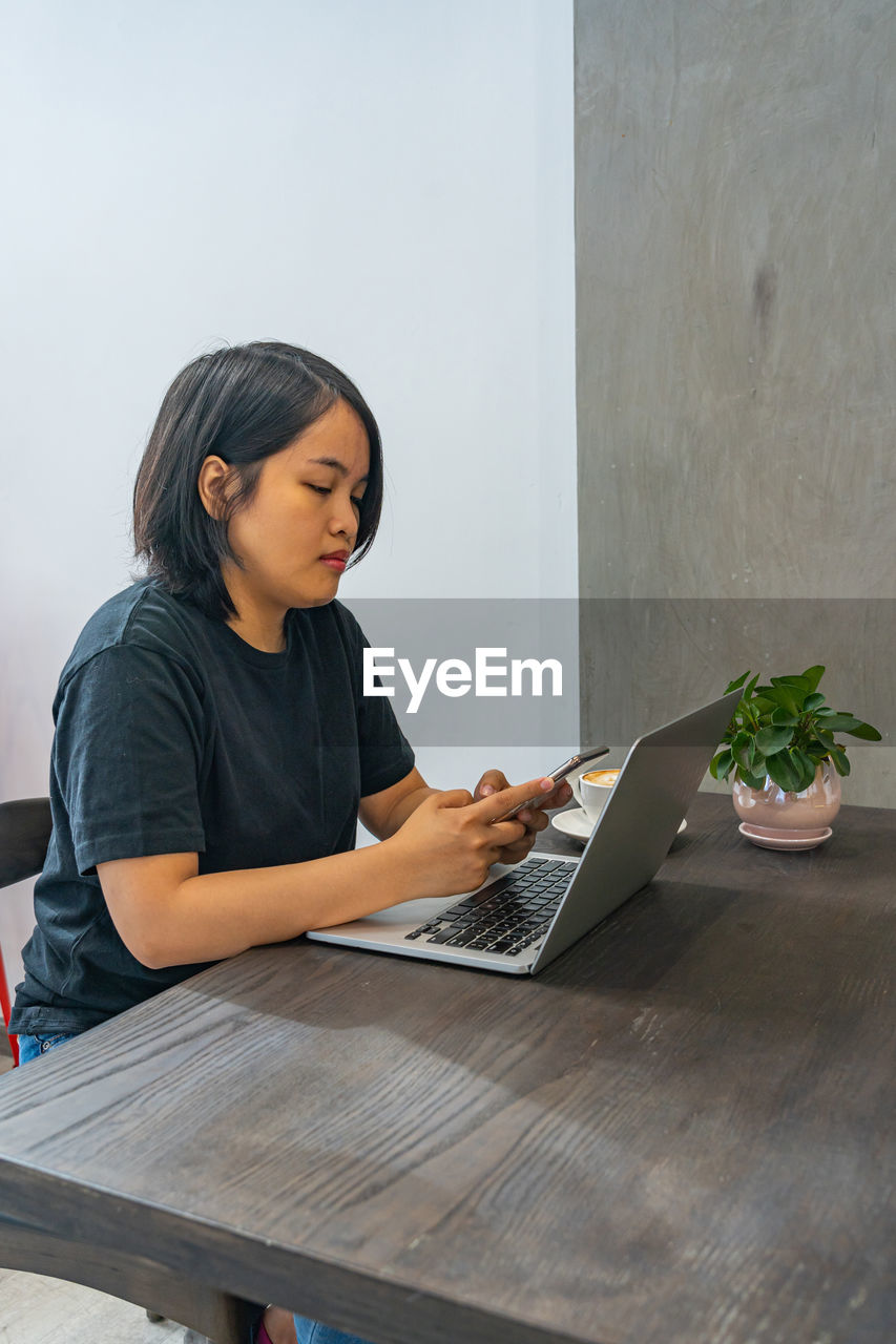 Young woman using phone while sitting on table