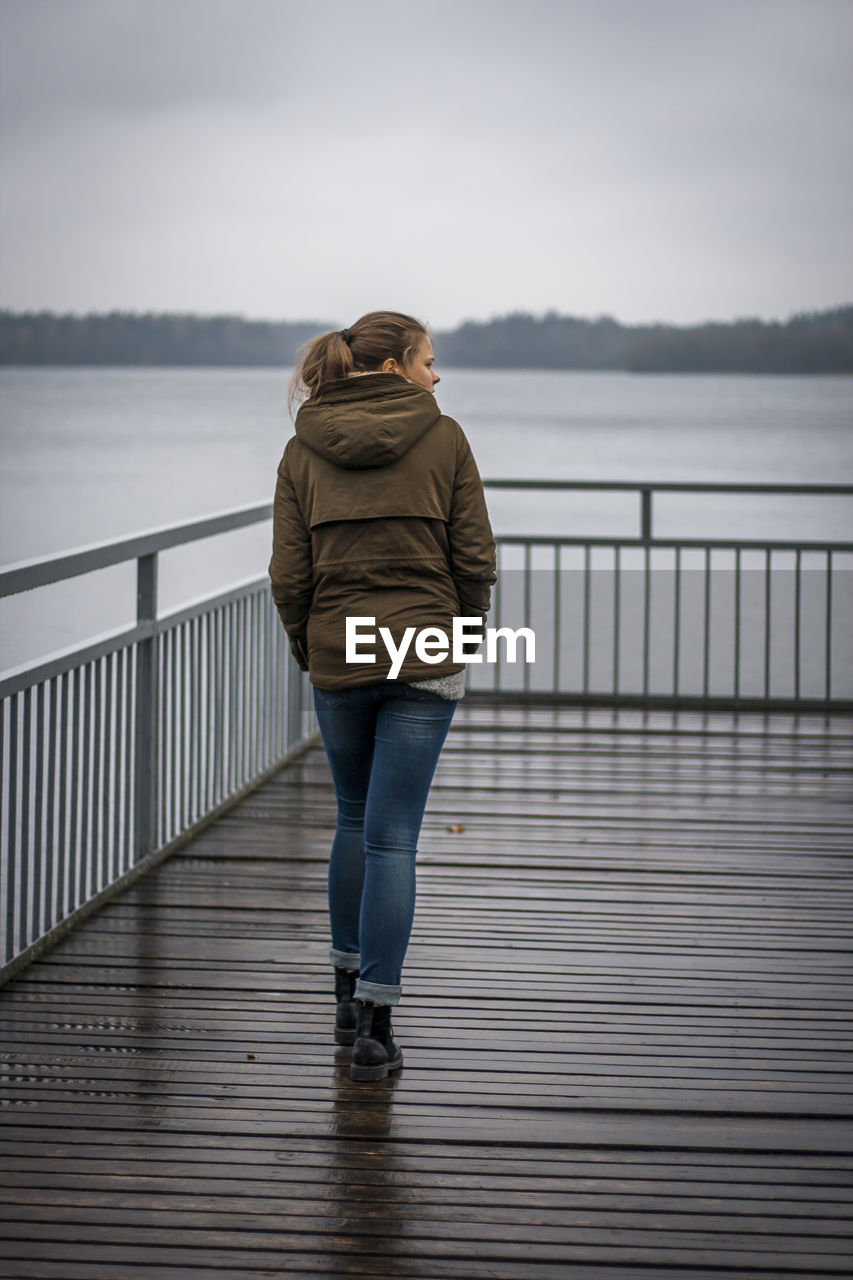 Rear view of woman walking on pier over lake against sky