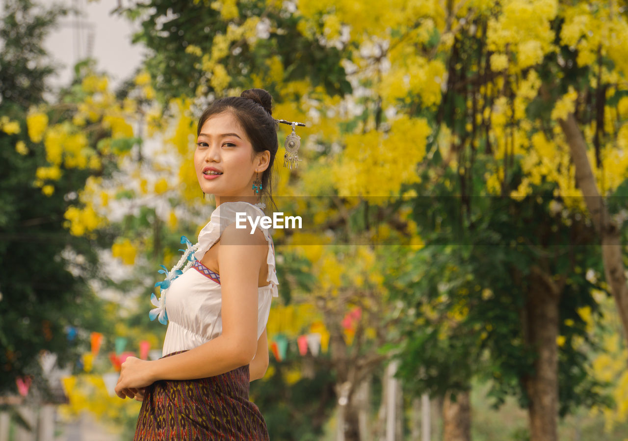 PORTRAIT OF SMILING WOMAN STANDING AGAINST YELLOW PLANTS