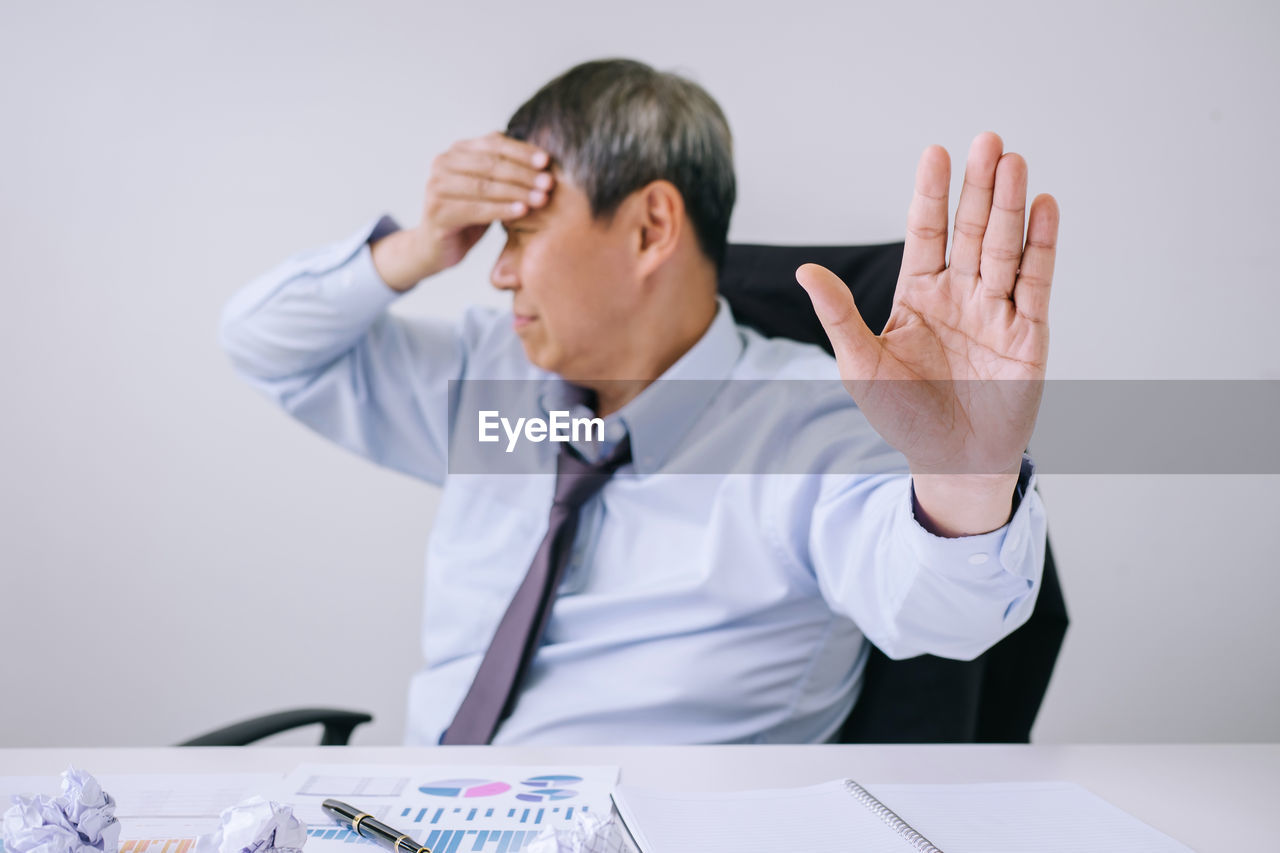 Businessman with headache sitting on chair while gesturing in office