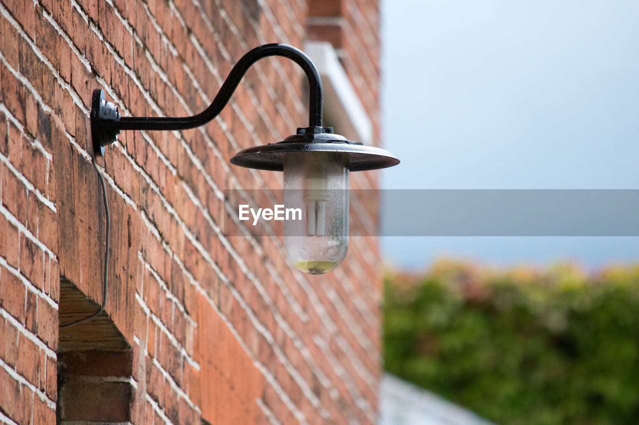 Low angle view of lighting equipment on brick wall against clear sky