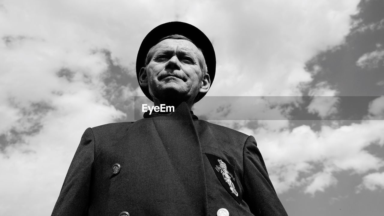 Low angle portrait of senior man wearing suit while standing against sky