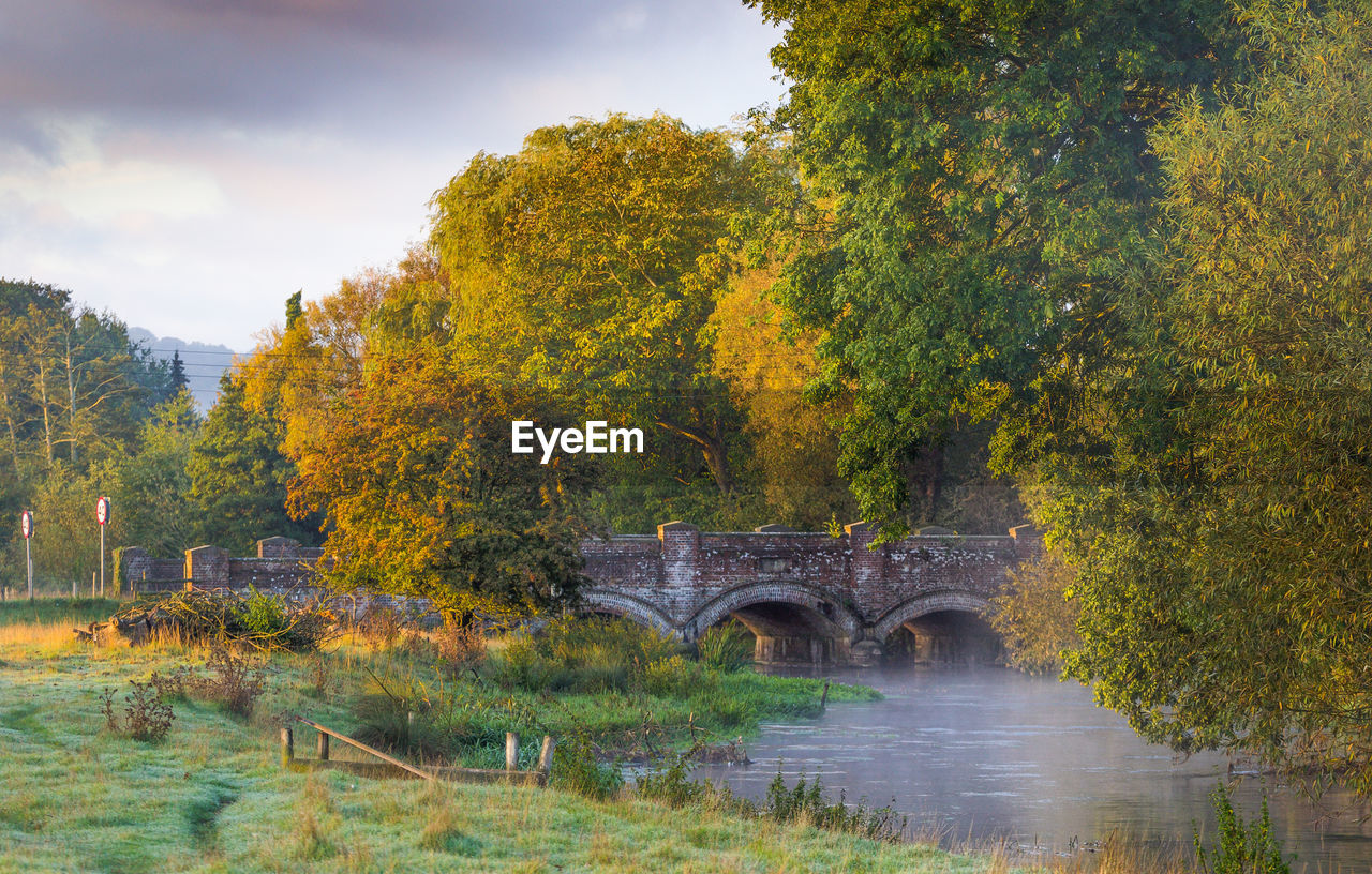 ARCH BRIDGE OVER RIVER AMIDST TREES AGAINST SKY DURING AUTUMN