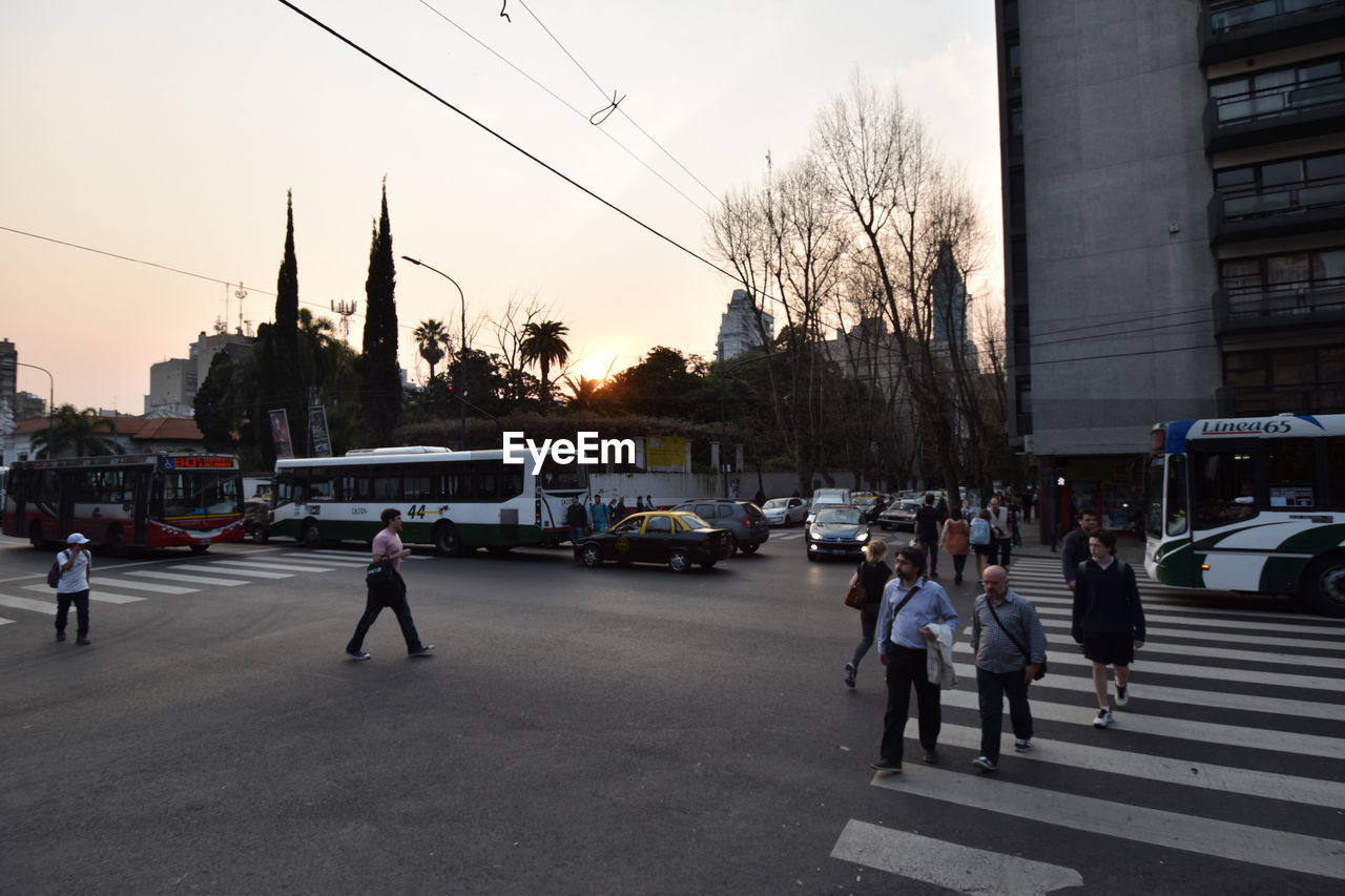 People on street in city against sky at sunset