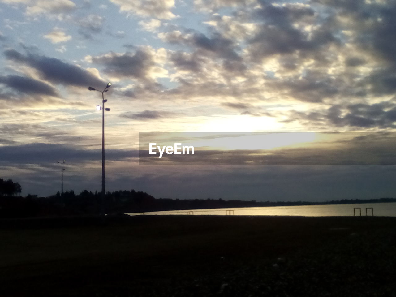 SILHOUETTE OF ELECTRICITY PYLON ON FIELD AGAINST SKY AT SUNSET