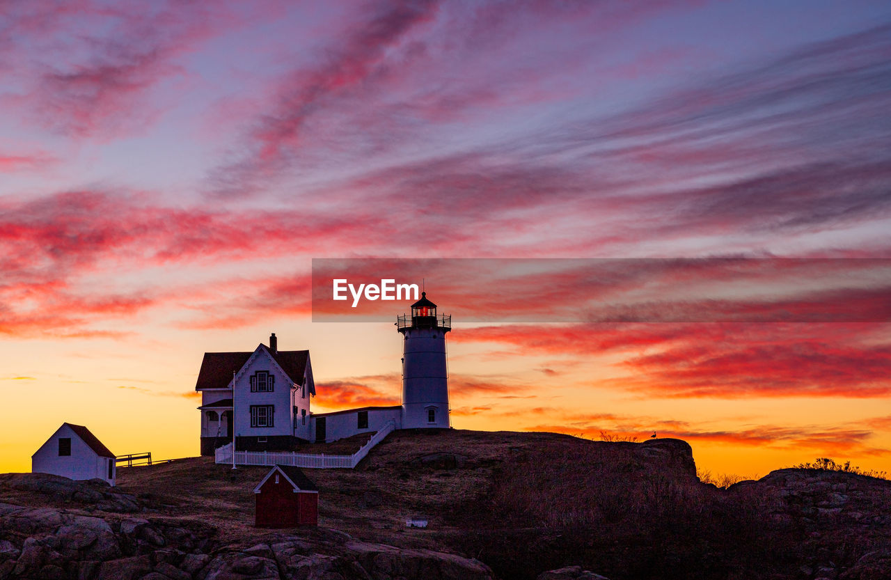 Lighthouse silhouette under a colorful red sky and clouds at sunrise.