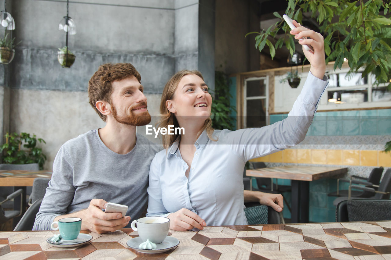 Cheerful couple doing selfie at cafe