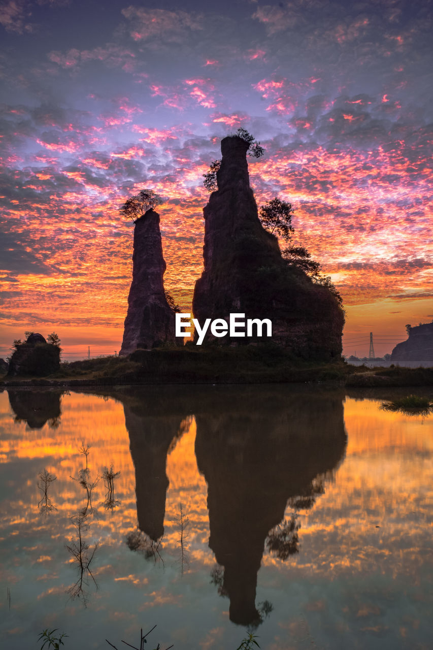 ROCK FORMATION ON LAKE AGAINST SKY DURING SUNSET