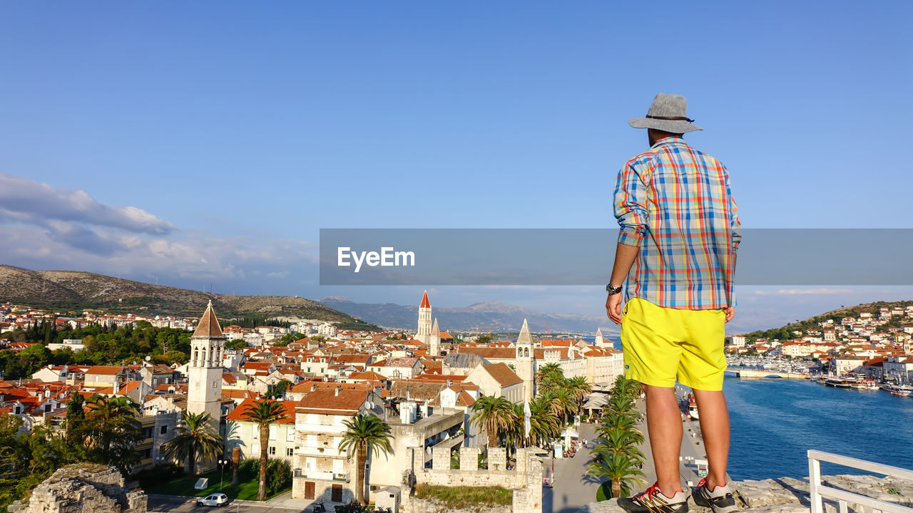 Rear view of man looking at cityscape against sky