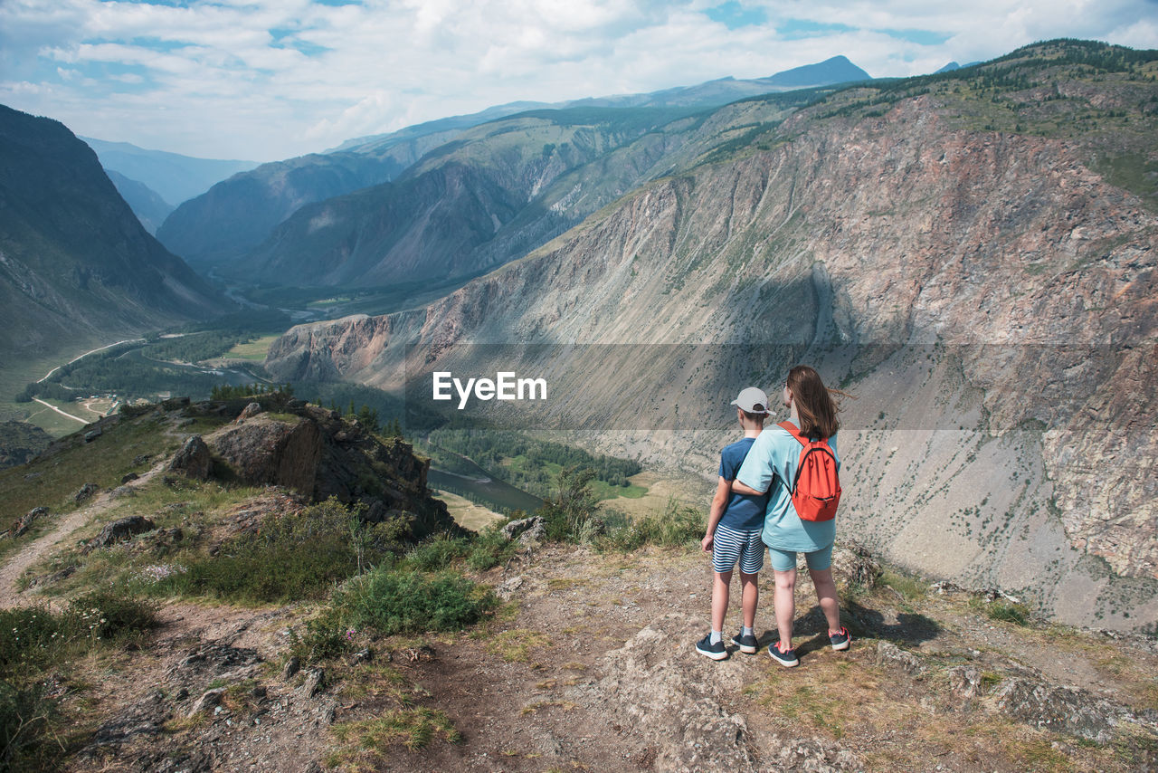 REAR VIEW OF MAN AND WOMAN LOOKING AT MOUNTAIN
