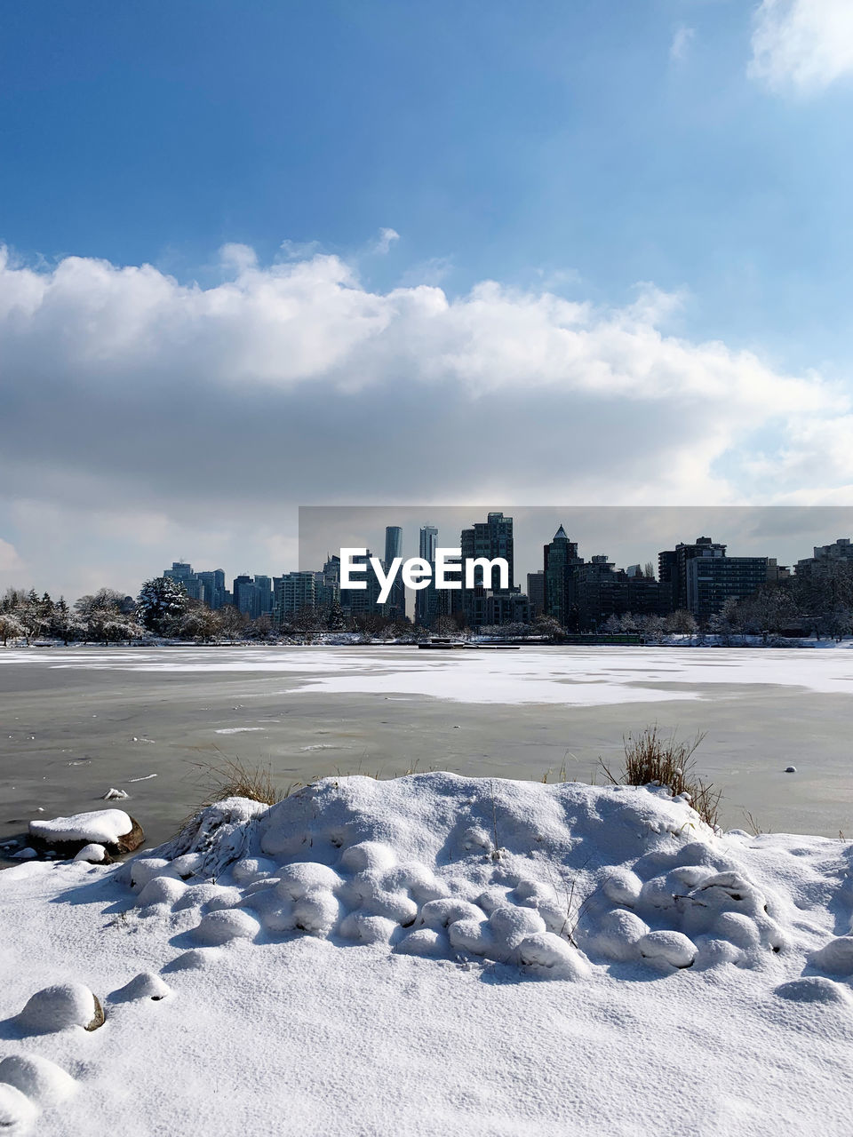 Frozen lake by buildings in city against sky