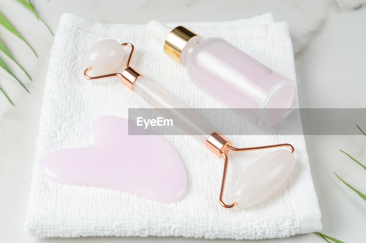 Pink quartz gua sha scraper and roller face massager and bottle of cosmetic serum for the face 