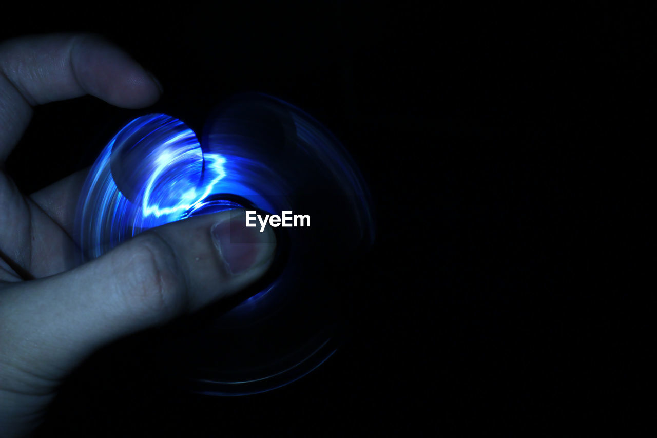 CLOSE-UP OF HAND HOLDING ILLUMINATED LIGHT OVER BLACK BACKGROUND