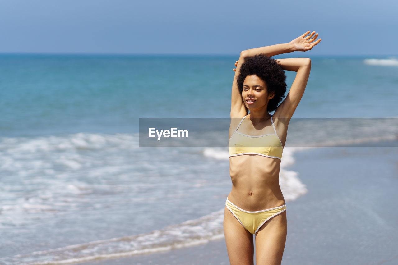 portrait of young woman wearing bikini while standing at beach