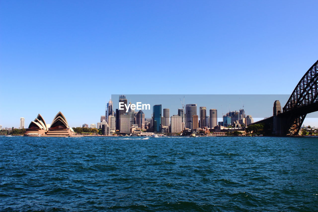 View of buildings by river against blue sky