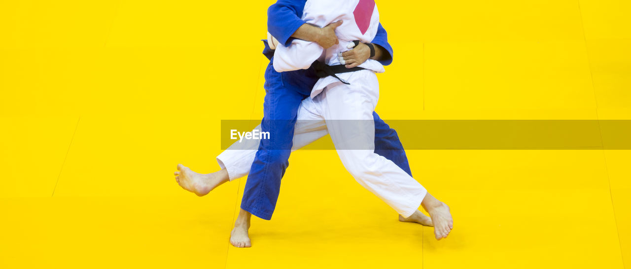Low section of people practicing martial arts against yellow background
